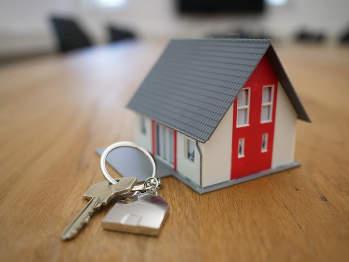 Model house with gray roof and red wall on a table beside a set of keys on a keychain.
