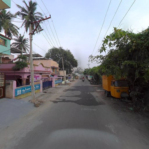 Narrow street in an Indian neighborhood with colorful buildings, parked auto-rickshaw, and tropical trees lining the road.