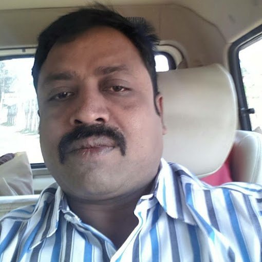 Man with a mustache in a striped shirt sitting inside a vehicle, looking at the camera.