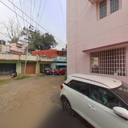 Street view of a white SUV parked near a pink building, with trees and shops in the background on a cloudy day.