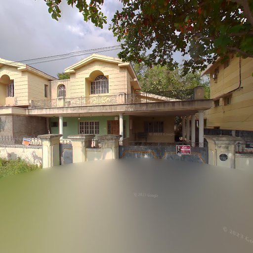Two-story beige house with a balcony and a small front yard, surrounded by a gated fence, under a partly cloudy sky.