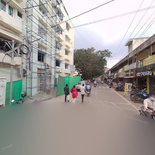Street scene with people walking, scaffolding on building, mopeds parked, and shops on the right. Overcast sky above.