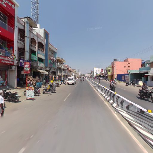 Busy urban street with vehicles, shops, and pedestrians on a sunny day. Buildings line both sides of the road.
