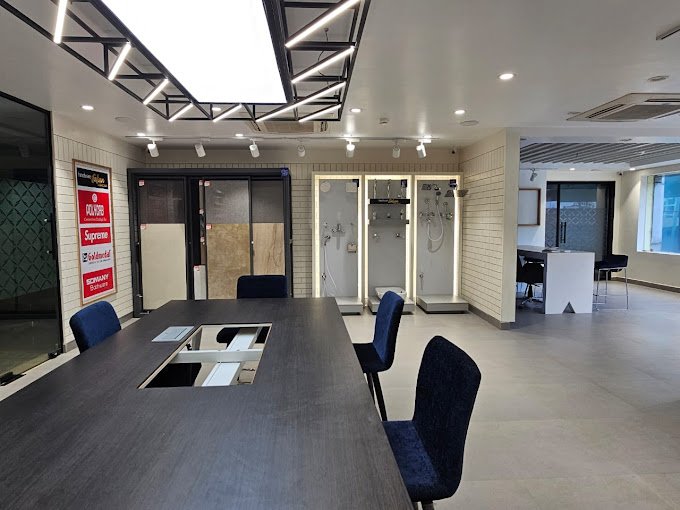 Modern showroom with display of bathroom fixtures, a large wooden table, and chairs under sleek lighting.