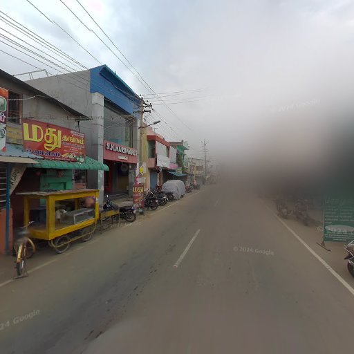 Street view of a row of shops with colorful signage and parked motorcycles on a hazy day, under a cloudy sky.