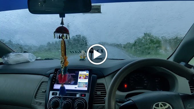 Car dashboard with decorations and a GPS, seen through a rainy windshield. Steering wheel visible.